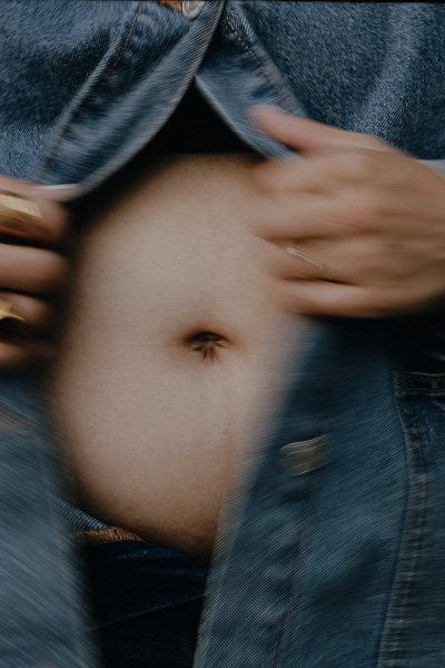 Woman opening a denim jacket to reveal her midriff