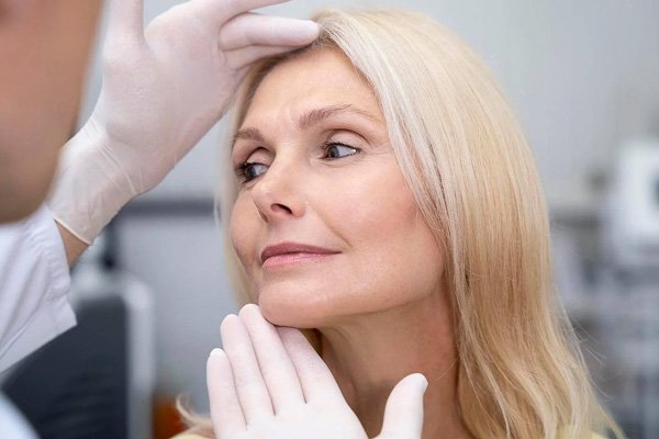 Doctor examining a woman's face with gloved hands